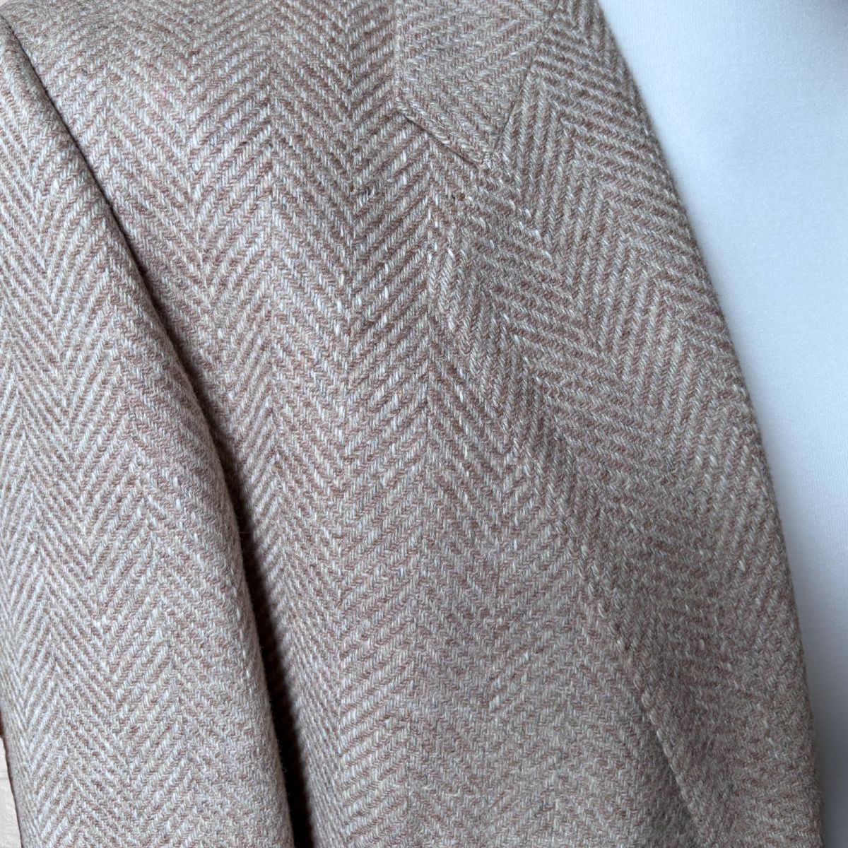 Close-up of a beige and brown herringbone patterned wool jacket draped over a white surface.