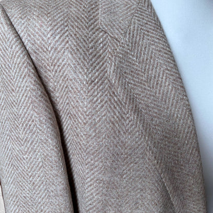 Close-up of a beige and brown herringbone patterned wool jacket draped over a white surface.