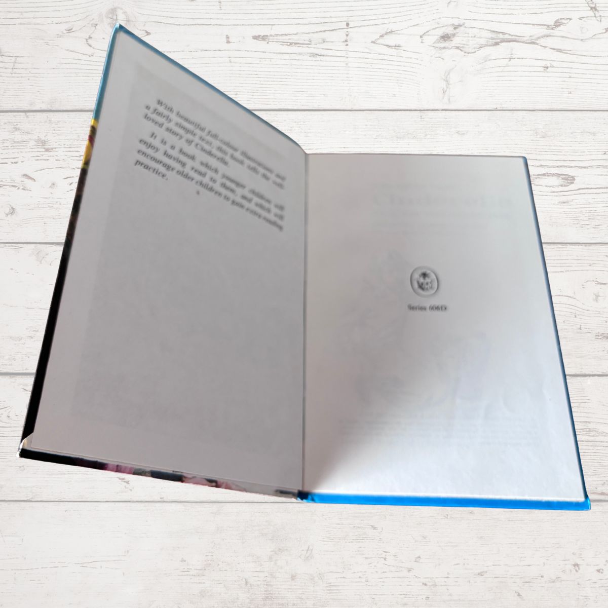 An open book with printed text on the left page and a small circular emblem on the right page, photographed from above on a white wood plank surface.