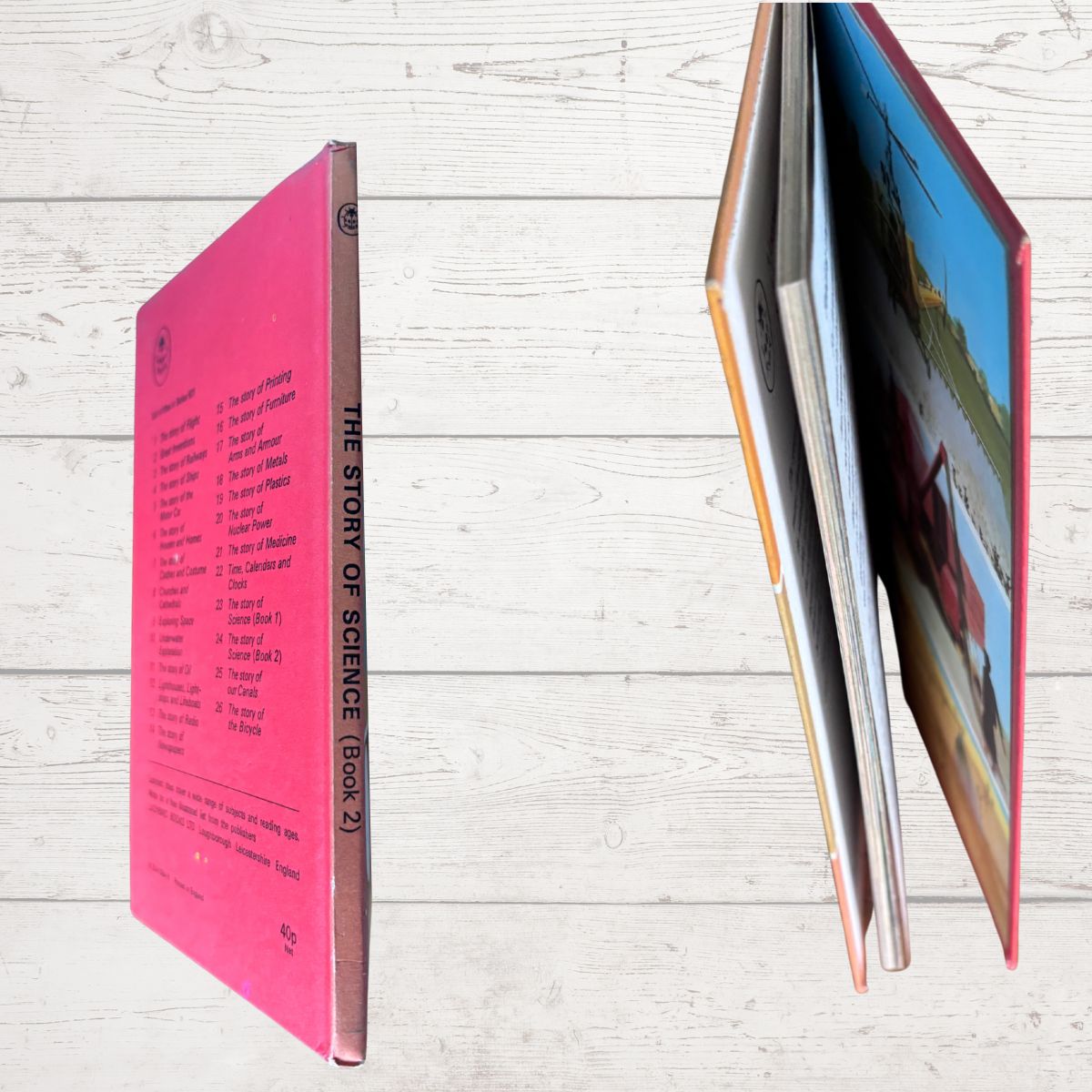 A hardcover book titled 'The Story of Science (Book 2)' shown from multiple angles on a light wood background. One view shows the bright pink back cover with black text, and another shows the open front cover with colorful scientific illustrations.