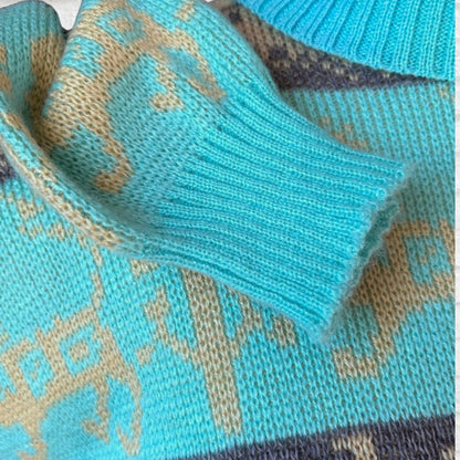 Close-up of a knitted sweater showing a ribbed cuff in bright turquoise with a beige fair-isle style pattern and hints of gray in the knit.