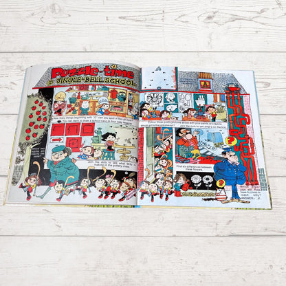 An open vintage children's puzzle book spread on a white wood plank surface, featuring colorful comic-style illustrations and the title 'Puzzle-time: A Single-Ball School.'.