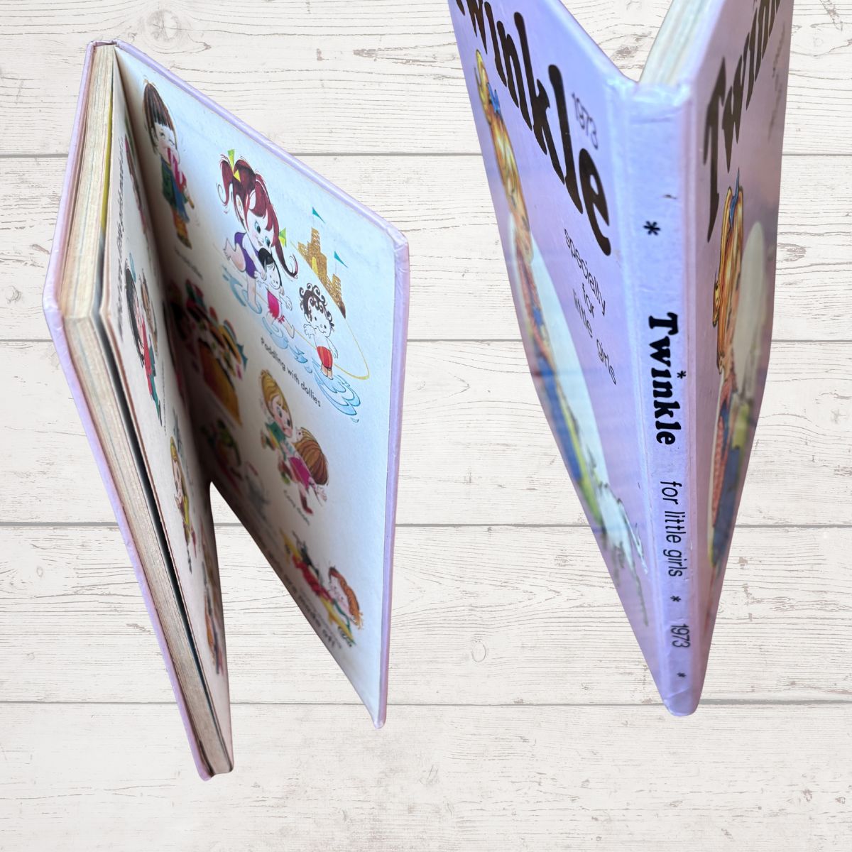 A children's hardcover book titled 'Twinkle' shown open and standing on a light wood plank surface. The cover and pages feature pastel illustrations of children and stars, with the title in large black text.