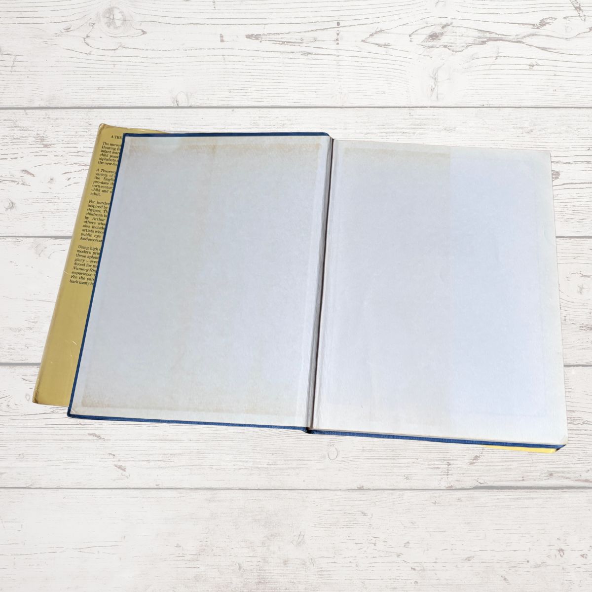 An open book with blank white pages and a tan cover, placed on a white wooden surface.