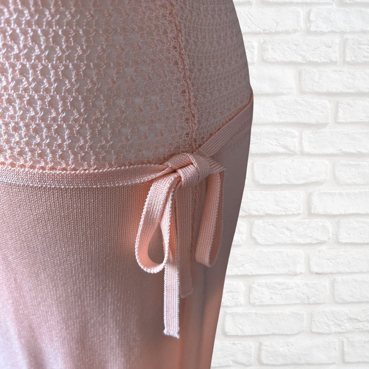 Close-up of a light pink dress  and side tie, shown against a white brick wall background.