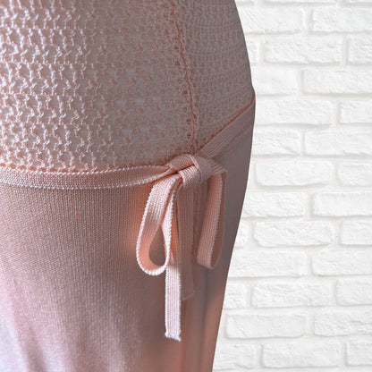 Close-up of a light pink dress  and side tie, shown against a white brick wall background.
