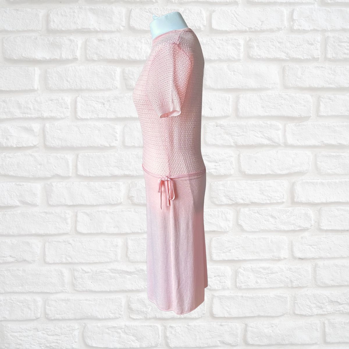 A light pink dress displayed on a mannequin torso against a white brick wall background.