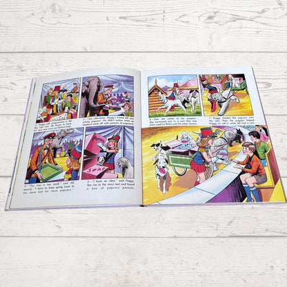 An open children's book with colorful comic-style illustrations spread across two pages, photographed on a light whitewashed wood surface.