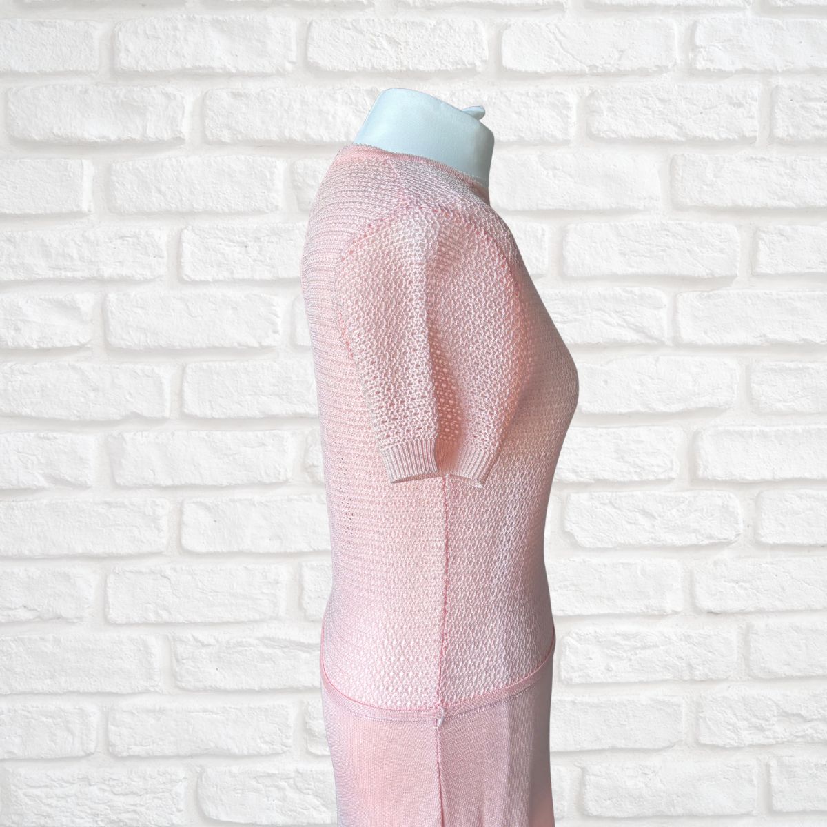 A light pink short-sleeve dress displayed on a white mannequin torso against a white brick wall background.