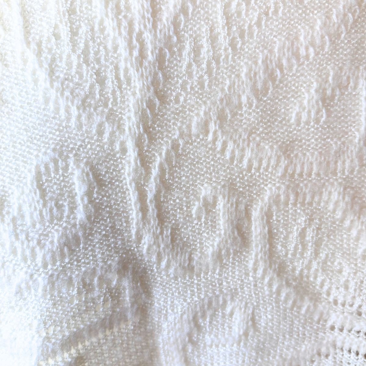 A close-up of a white textured knit fabric with a detailed lace-like pattern.