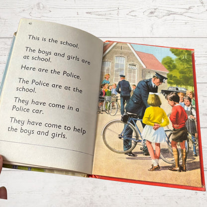 Open book with a vintage illustration of a police officer and children on a school day.