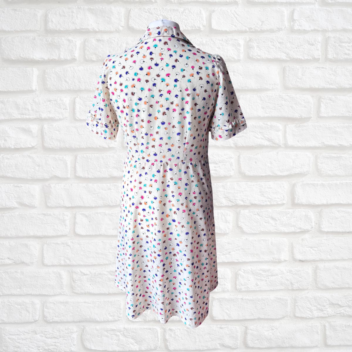 Short-sleeve dress with colorful polka dot pattern on a white brick wall background