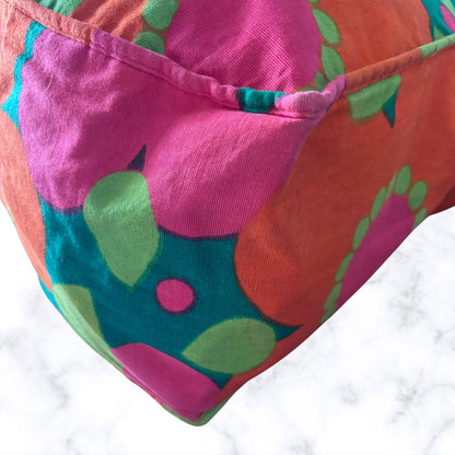 A close-up of a bag with a bold retro floral pattern in pink, orange, teal, and green, resting on a white marble surface.