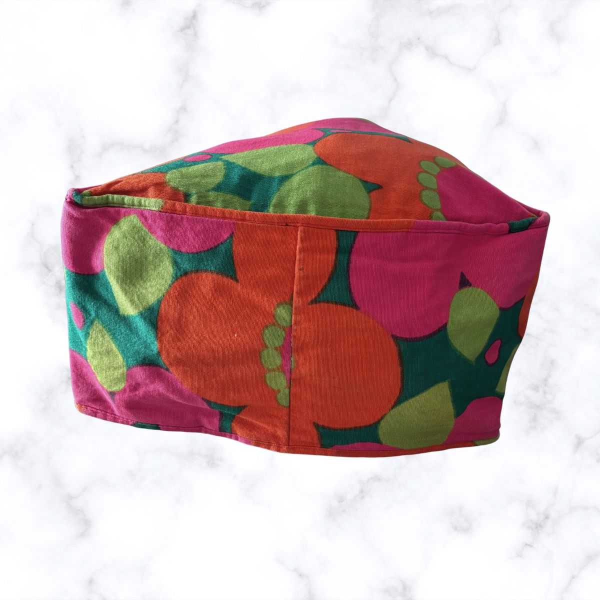 A fabric bag with a retro floral pattern in pink, orange, green, and teal, displayed on a white marble background.