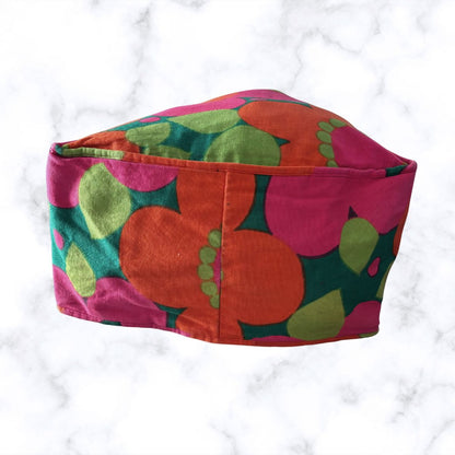 A fabric bag with a retro floral pattern in pink, orange, green, and teal, displayed on a white marble background.