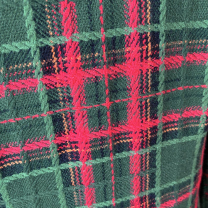 A close-up of a tartan plaid fabric pattern featuring dark green, vibrant red, and thin orange stripes.