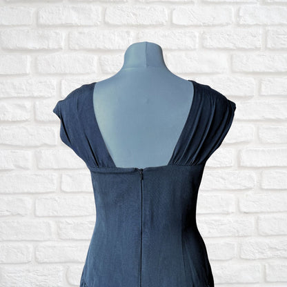 A black  sleeveless dress displayed on a matching mannequin torso, shown from the back against a white brick wall background.