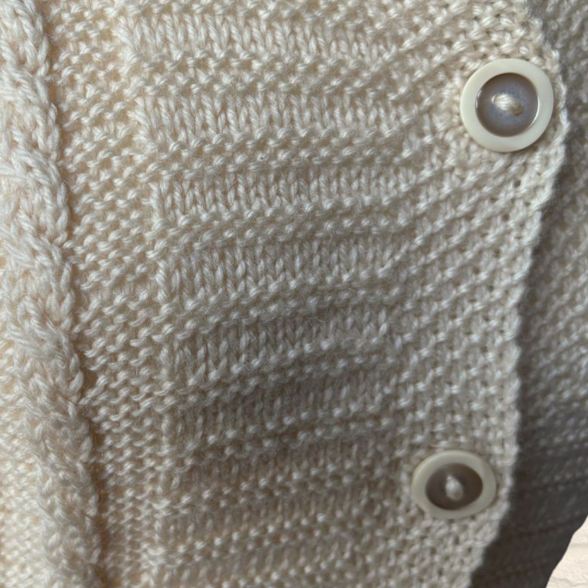 Close-up of a cream-colored knitted cardigan featuring textured knit patterns and decorative buttons.