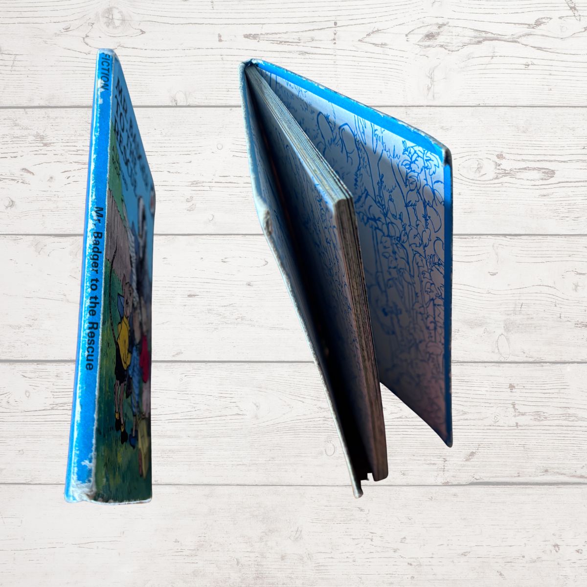 A hardcover book shown from two angles on a light wood plank background. One view shows the blue spine with the title 'My Paper to the Press' in white text, and the other shows the open blue-edged pages with illustrated covers.