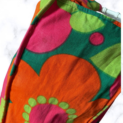 A close-up of a colourful patterned bag  featuring a retro floral design in orange, green, pink, and yellow on a white marble background.