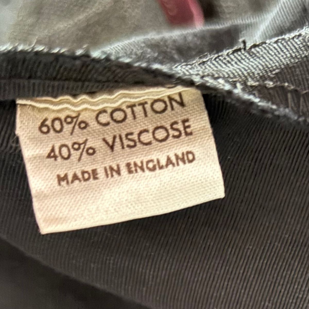 Close-up of a garment's inner neck label reading '60% COTTON 40% VISCOS MADE IN ENGLAND' on a dark charcoal fabric.