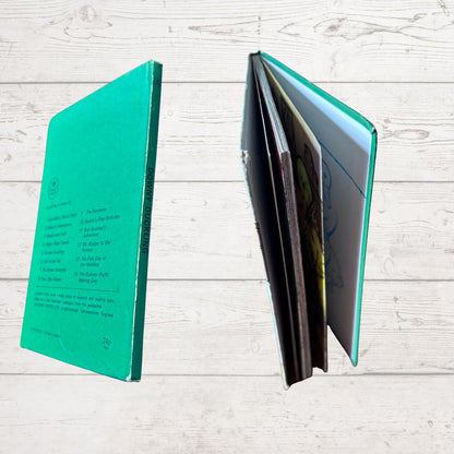 A hardcover notebook with a bright teal-green cover shown from both the front cover and the open interior pages, set against a light whitewashed wood plank background.