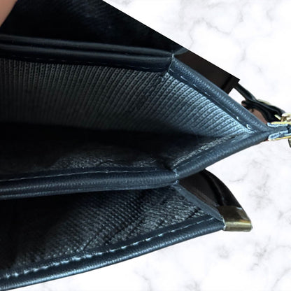 Close-up of the interior of a black textured leather pouch or wallet, showing stitched edges, interior compartments, and a small gold-toned metal zipper pull on a white marble surface.