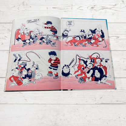 An open vintage comic book laid flat on a white wood surface, showing four-panel cartoon scenes with red, black, white, and pink tones.