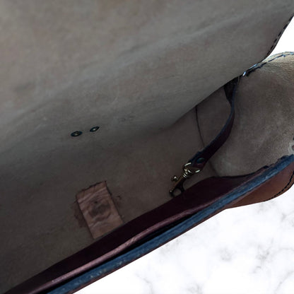 Close-up of the interior of a brown leather bag, showing the lining, a dark strap with a metal clasp