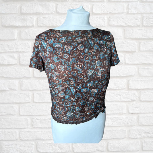 A short-sleeve blouse with a brown, blue, and beige paisley pattern, displayed on a light blue mannequin torso against a white brick wall background.