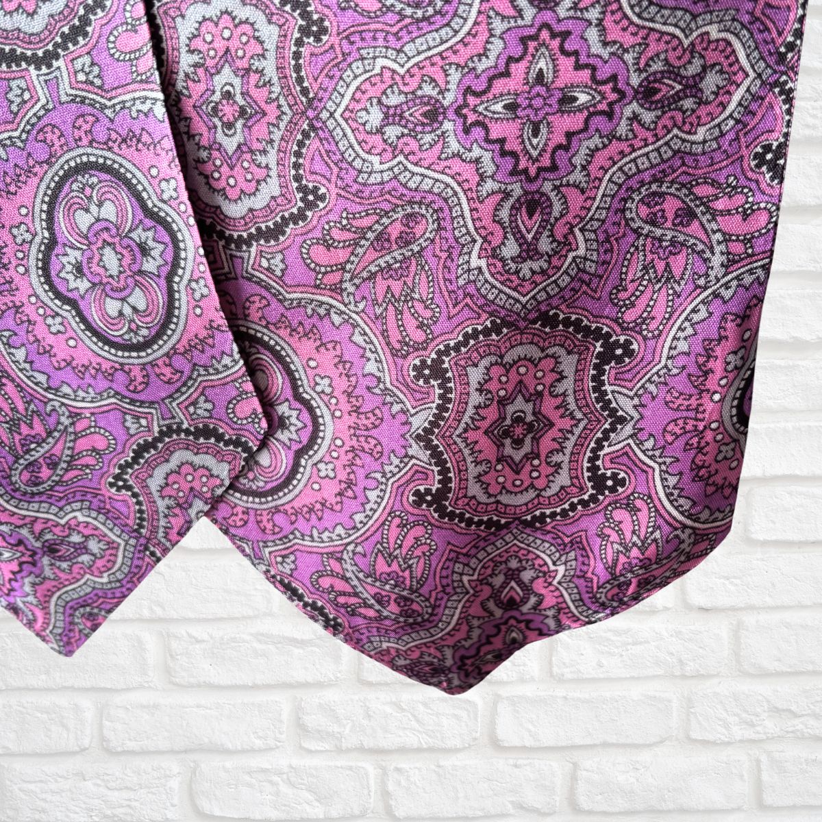 Close-up of a pink and black paisley patterned fabric on a white brick wall background