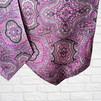 Close-up of a pink and black paisley patterned fabric on a white brick wall background