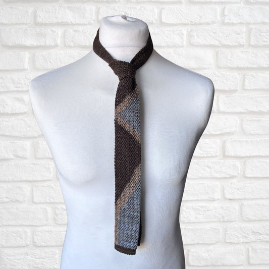 Knitted tie  with a geometric pattern on a mannequin against a white brick wall.
