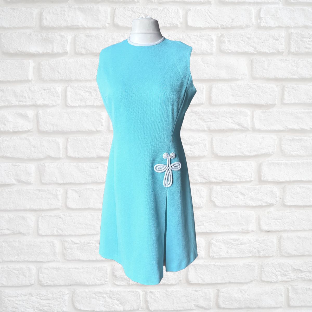 Light blue dress with a white emblem on a white brick wall background