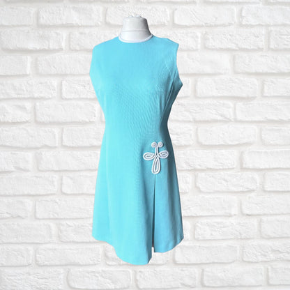 Light blue dress with a white emblem on a white brick wall background