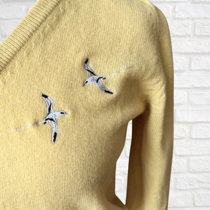 Yellow sweater with bird embroidery on a white brick wall background