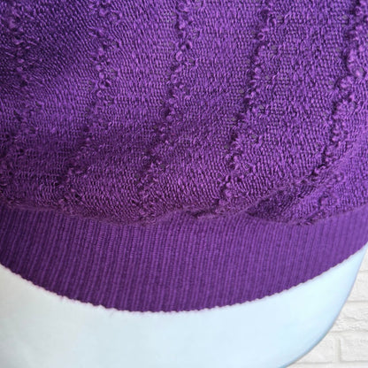 Close-up of a purple knit sweater  with a ribbed brim, shown on a white mannequin head against a light background.