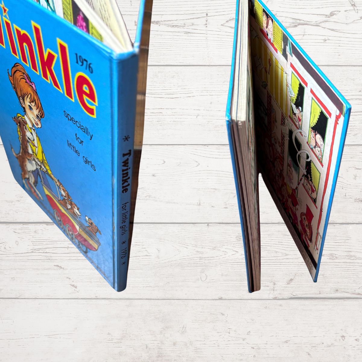 A children's hardcover book titled 'Tinkle 1976' shown standing open on a light wood floor, with the front cover and inner illustrated pages visible.