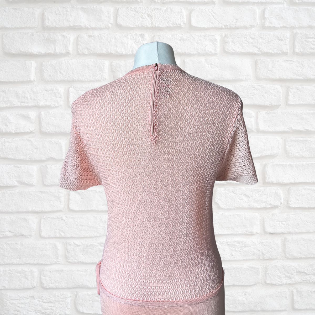 A light pink short-sleeve dress displayed on a mannequin torso, shown from the back against a white brick wall background.