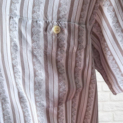 Close-up of a short-sleeve button-up shirt with vertical stripes in brown, beige, and white, featuring a decorative floral border between the stripes and a single cream-colored button on the chest pocket.