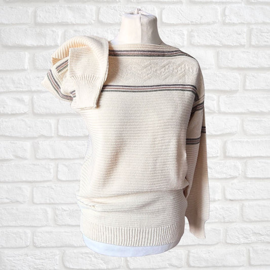 A cream-colored knit sweater with thin dark stripes across the chest and sleeves, displayed on a dress form mannequin against a white brick wall background.
