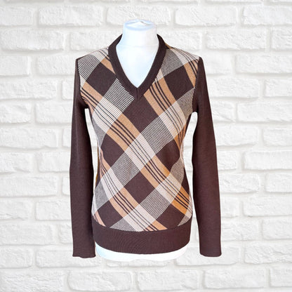 A brown long-sleeve V-neck sweater displayed on a white mannequin torso against a white brick wall background. The sweater features a brown, beige, and white plaid pattern across the chest and shoulders.