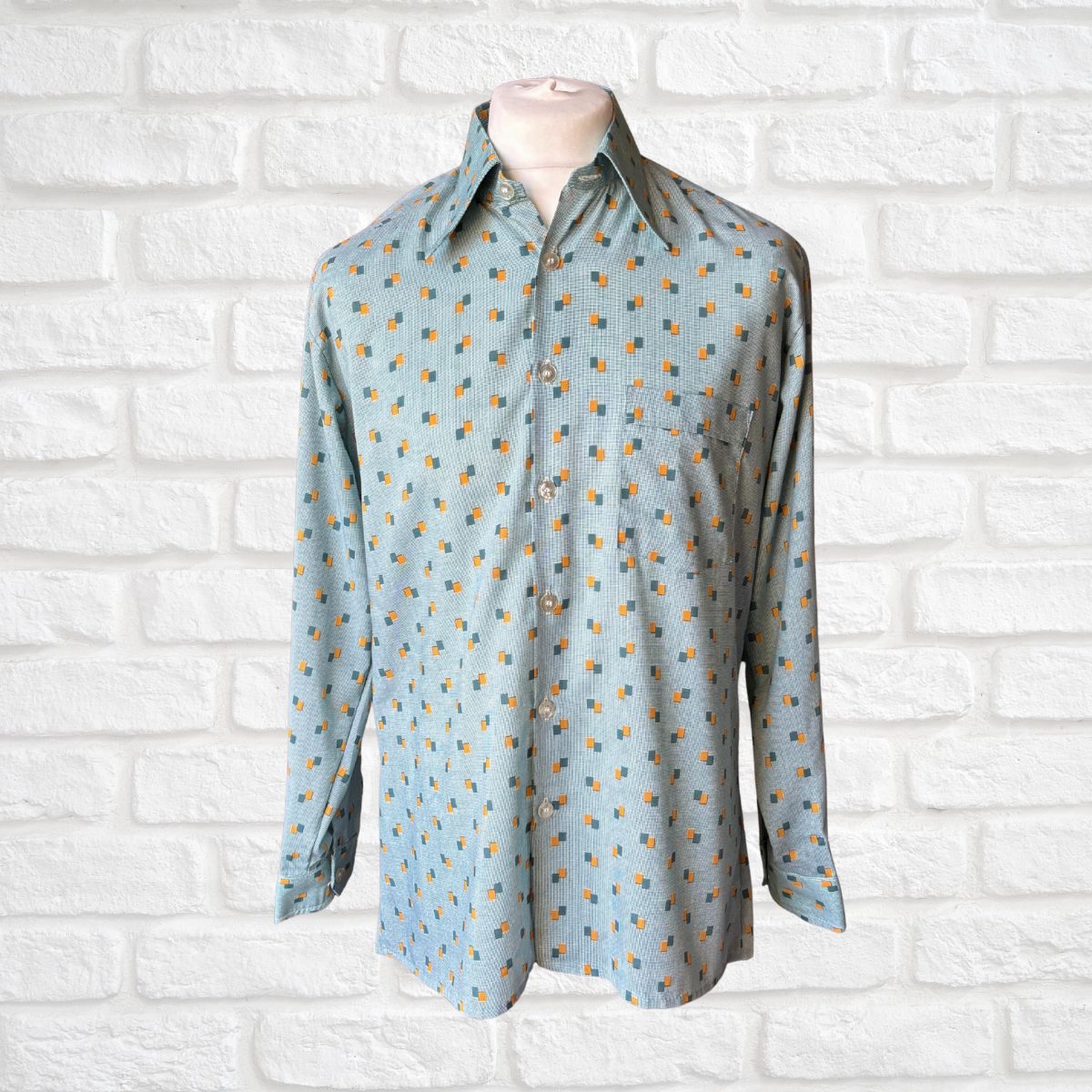 Light blue shirt with a bold  pattern on a mannequin against a white brick wall.