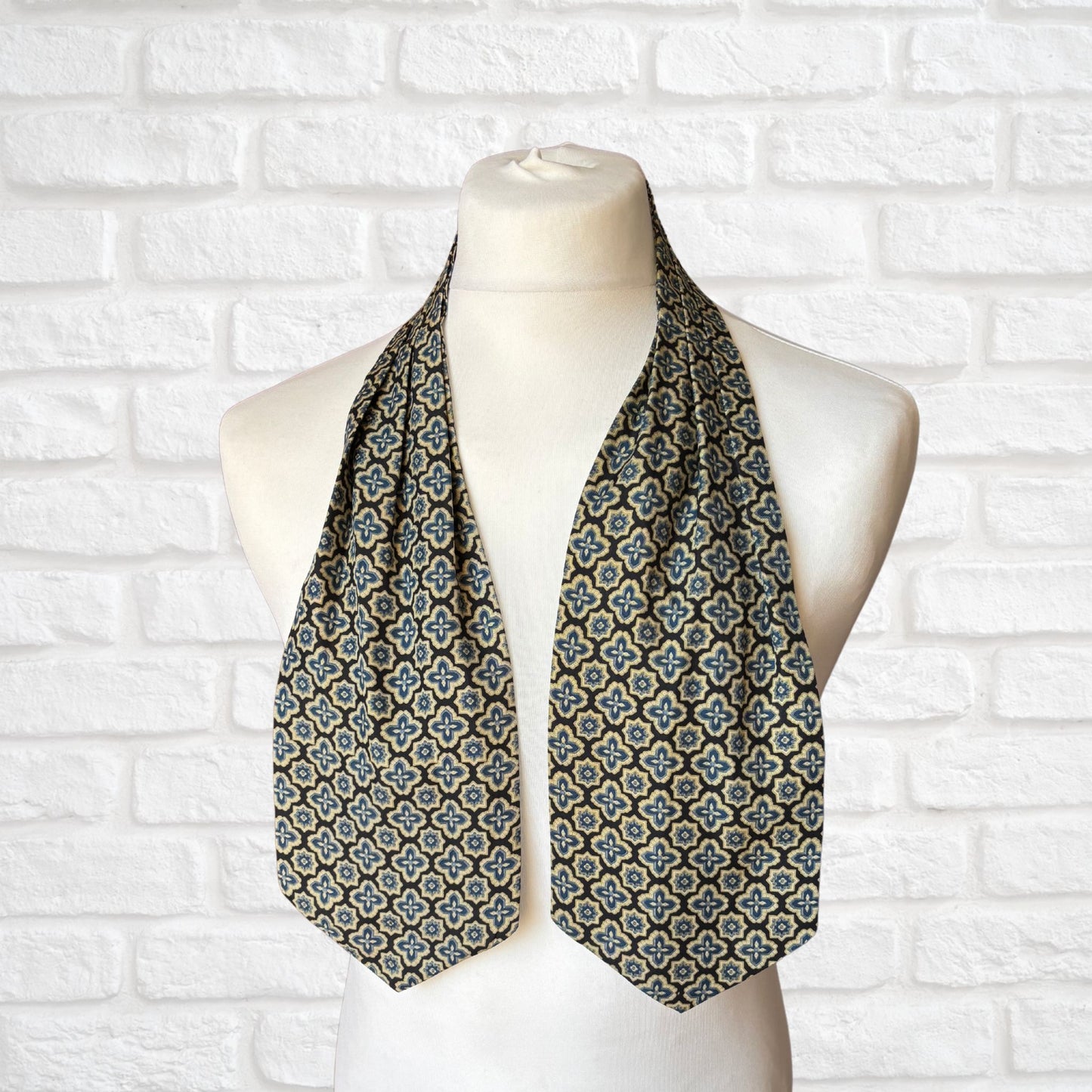 A vintage Austin Reed cravat featuring a black necktie with a cream, gold, and blue stylized floral print, displayed on a mannequin against a white brick wall background.