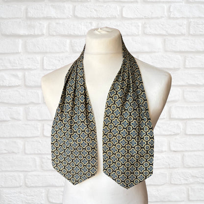 A vintage Austin Reed cravat featuring a black necktie with a cream, gold, and blue stylized floral print, displayed on a mannequin against a white brick wall background.