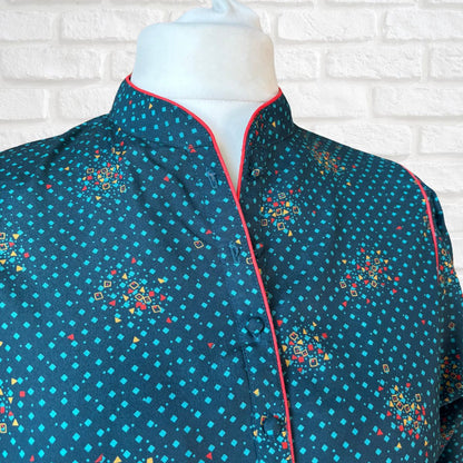 Mannequin wearing a blue patterned dress with red trim against a white brick wall.