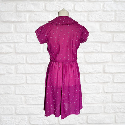Pink dress with white patterns on a mannequin against a white brick wall background