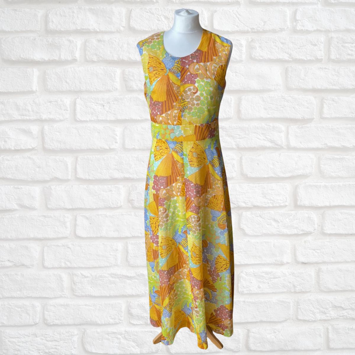 Colorful patterned dress on a mannequin against a white brick wall.