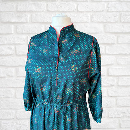 Teal dress with geometric pattern on a mannequin against a white brick wall.