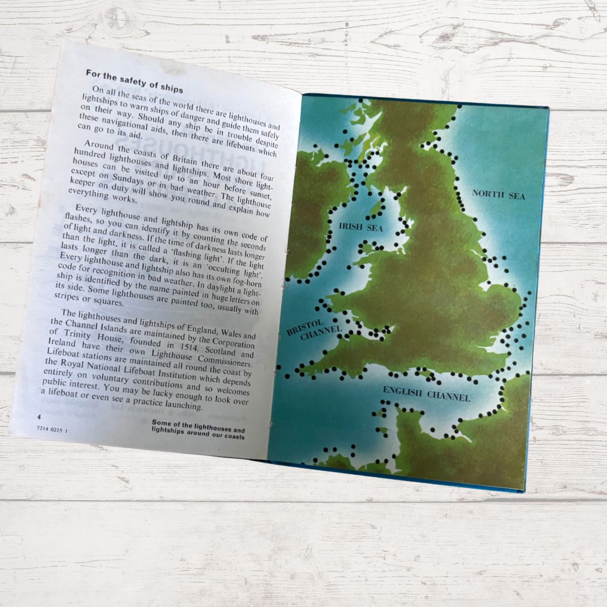 An open children's book spread showing a page with text about lighthouses and a map of the British Isles with lighthouses marked in green dots, placed on a light wood surface.